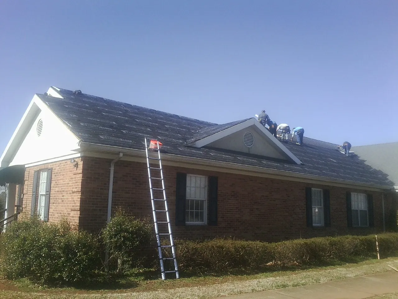 Crew tearing shingles off a brick ranch roof with a ladder set — Metal Roof Repair work by our crew in Ahsahka
