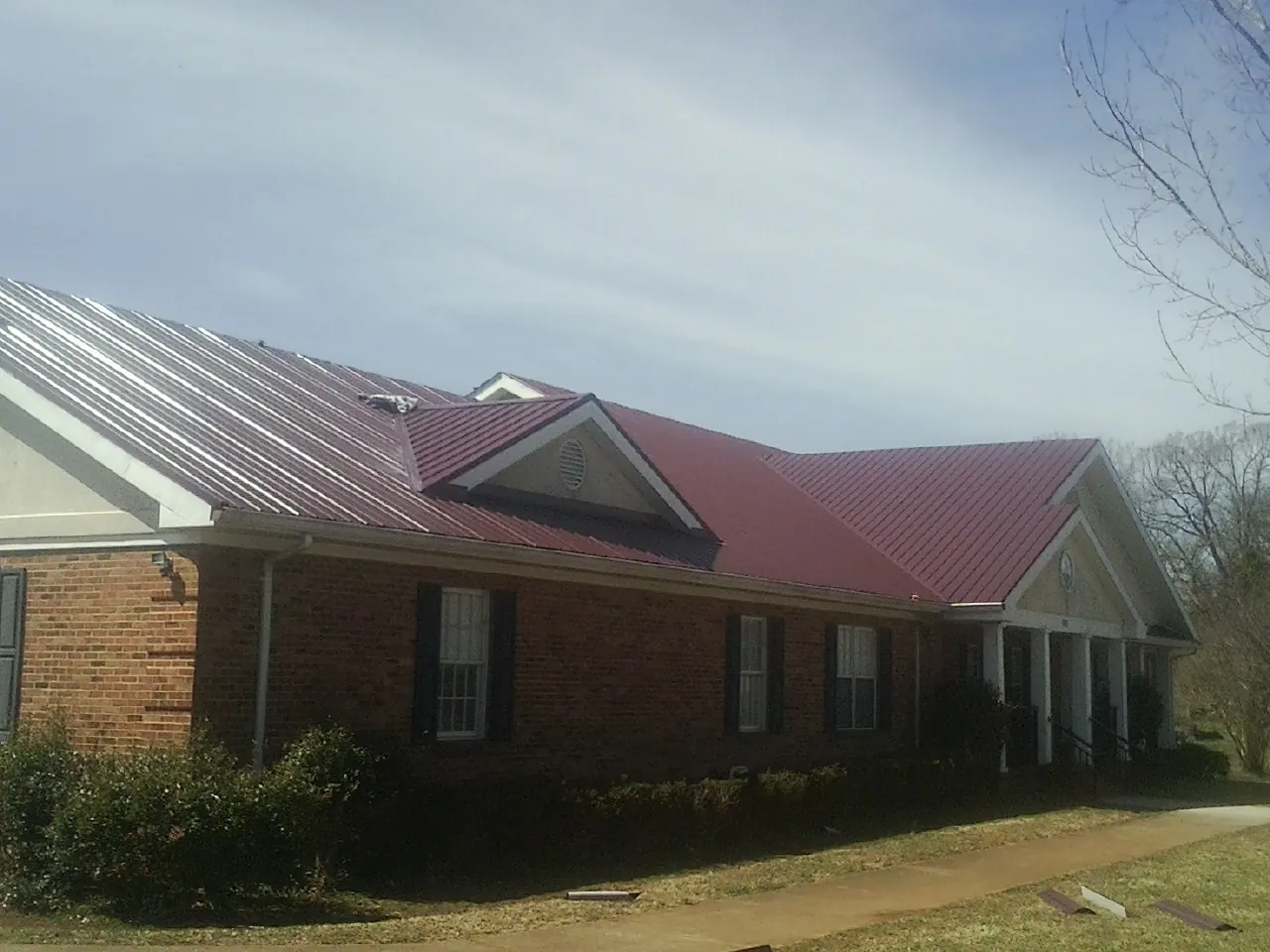 Red metal roof with gabled entries on a long brick building, from a Hail Damage Roof Repair job in Ahsahka