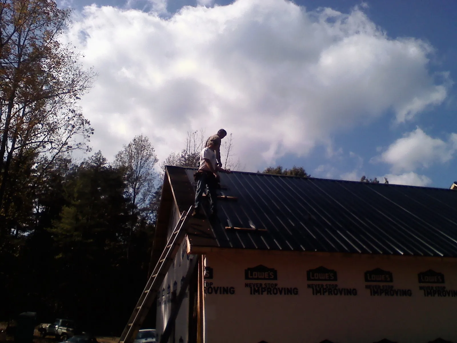 Roofer fastening dark metal panels high against a cloudy sky, from a Roof Inspection job in Ahsahka